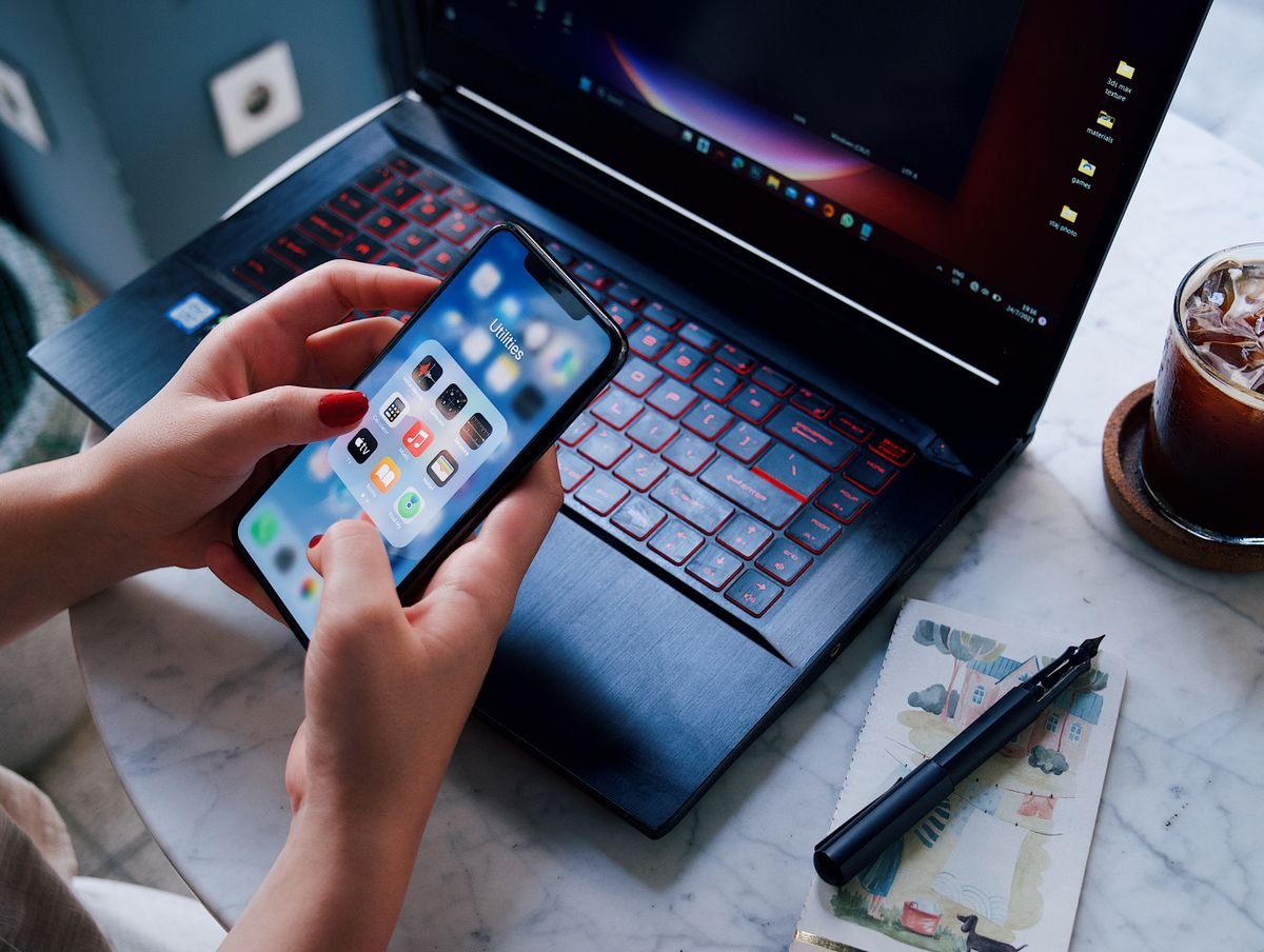 Mains tenant un smartphone au-dessus d'un ordinateur portable